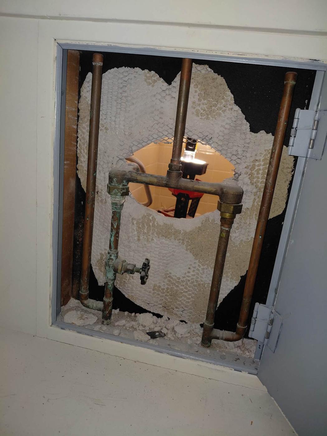 Old pipework seen through an open wall access panel before the valve was replaced